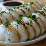 Freshly cooked Yuanbao dumplings served on a plate with green onions and sesame seeds, paired with soy sauce, symbolizing a classic Chinese recipe.